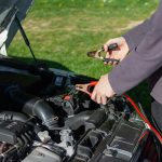 Close-up of mechanic using jumper cables to jump-start a car battery outdoors.